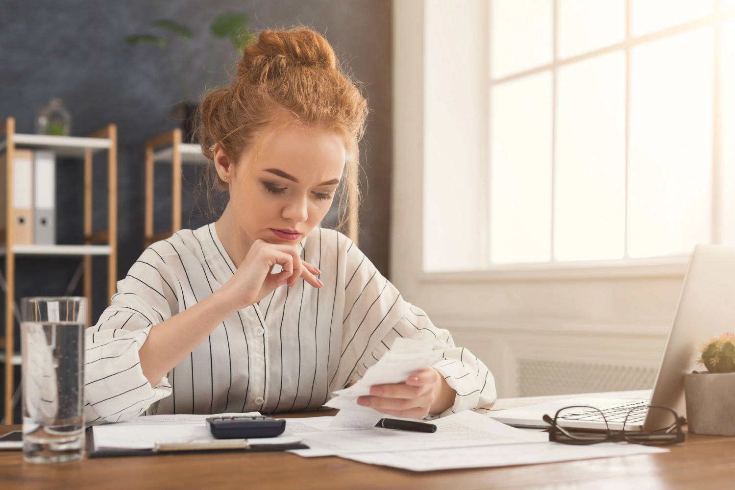 A young business owner reviewing receipts and documents at her desk, calculating expenses for tax deductions.